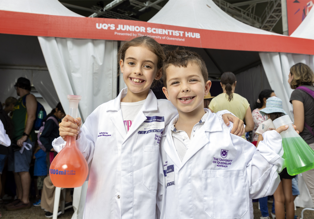 Two Junior Scientists in lab coats holding science props at IMB's Junior Science Hub