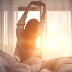 A woman wakes in the morning and stretches while being bathed in morning light
