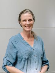 Wendy Mansell in a blue shirt standing in front of a grey background