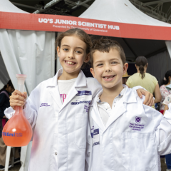 Two Junior Scientists in lab coats holding science props at IMB's Junior Scientist Hub