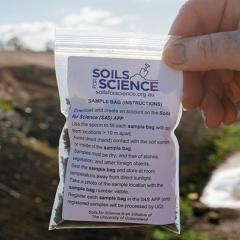 Hand holding up Soils for Science sample bag with field in the background