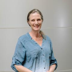 Wendy Mansell in a blue shirt standing in front of a grey background